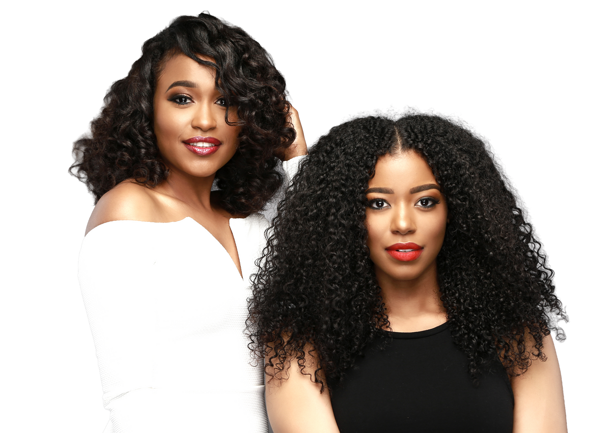 Two women posing with voluminous, curly black hair extensions or wigs against a solid white background. One woman wears a white off-the-shoulder top and the other wears a black top.